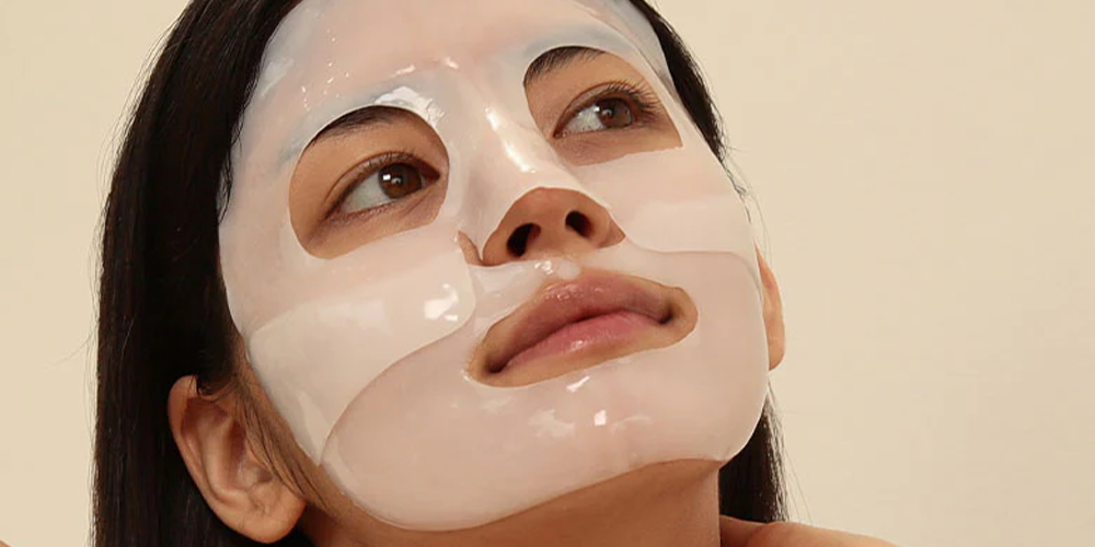 Close-up of a person with straight dark hair against a plain beige background for a sheet mask skincare article